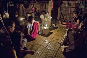 a family of thailand's hilltribe people are sitting on the floor a bamboo house and a candle is lit and placed in the middle of the room