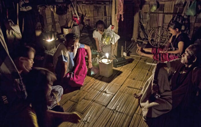 a family of thailand's hilltribe people are sitting on the floor a bamboo house and a candle is lit and placed in the middle of the room