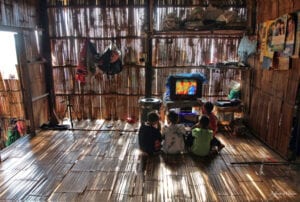 northern thailand hilltribes - jeffrey warner - development- culture change - lahu youth watching color television while in a bamboo house
