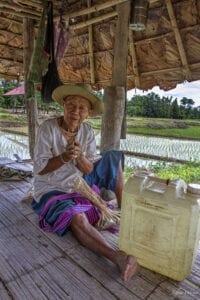 kabuwa, an indigenous karen hilltribe man, is sitting on the floor; he wearing traditional karen pants and a straw hat 