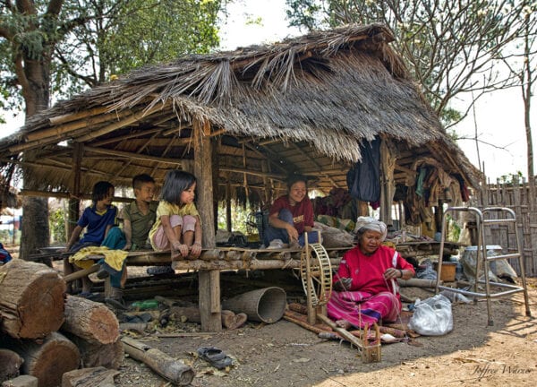 several generations of nam bor noi karen village are sitting in a bamboo hut and watching an elder weave